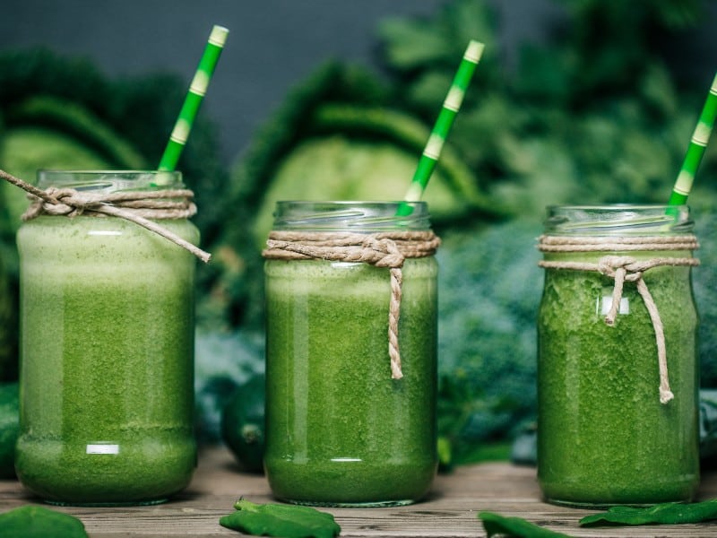 Three mason jars filled with green smoothies and green straws