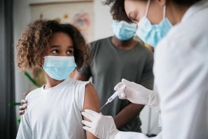 A child in a mask receiving a vaccine from a medical professional