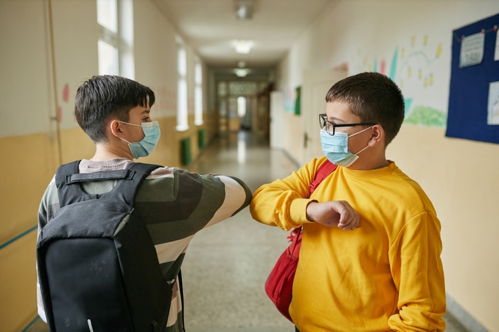 Two kids in masks bumping elbow when they are back to school