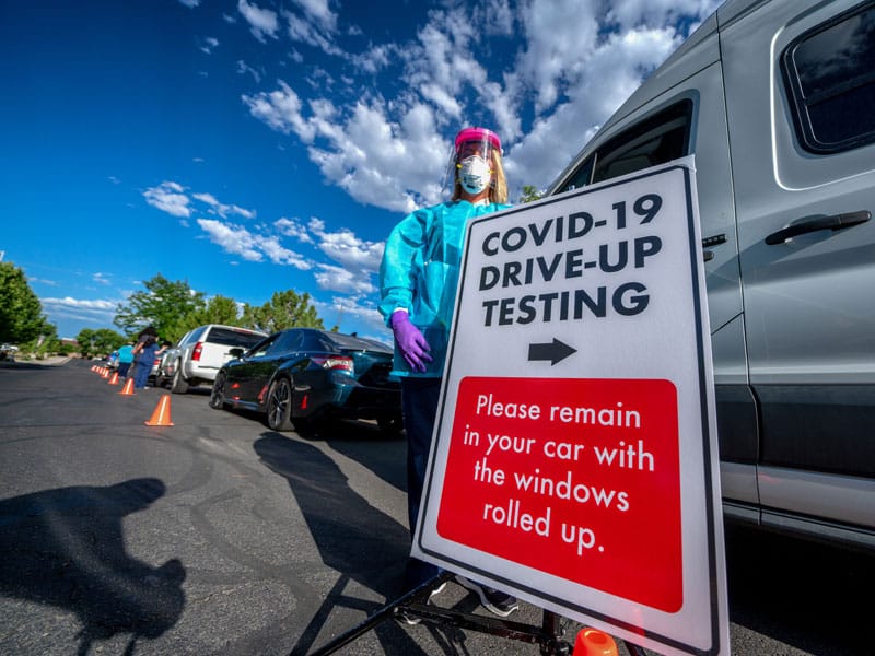 Sign of a COVID-19 test center with the text "COVID-19 drive up testing" and instructions to remain in cars with windows rolled up"