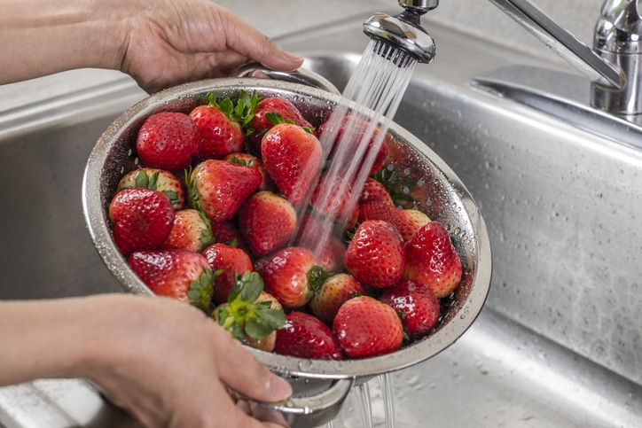 Strawberries under running water in a bowl in a sink