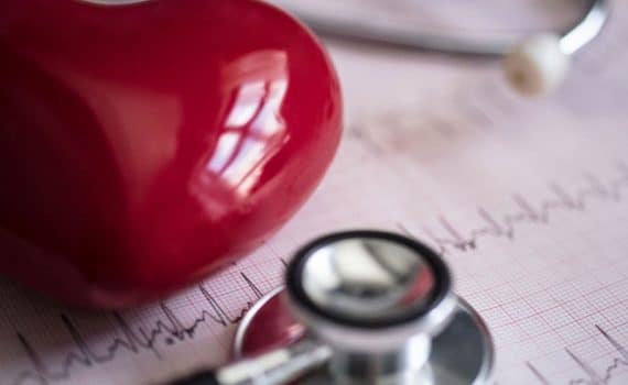 A red heart paper weigh resting on top of papers with a stethoscope near by, used to explain reversing heart disease