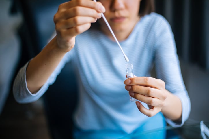 Woman in a blue blouse placing a nose swab into a testing vial 