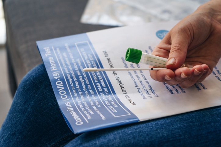 Person holding swab and reading a COVID-19 at-home test kit instructions