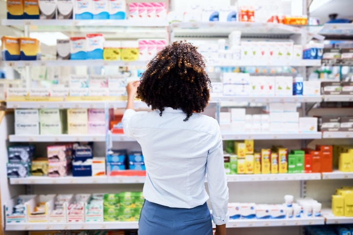 Woman in white blouse looking at a wall of medications