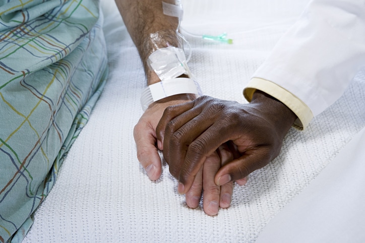 Two hands holding, likely a hospital patient in a gown and a doctor in a white coat