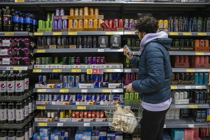 A man shopping in a grocery store checks the label on an energy drink.