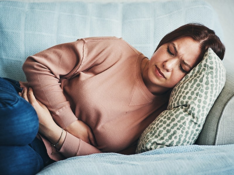 Woman in pink blouse clutching at abdomen, used to explain gallstones