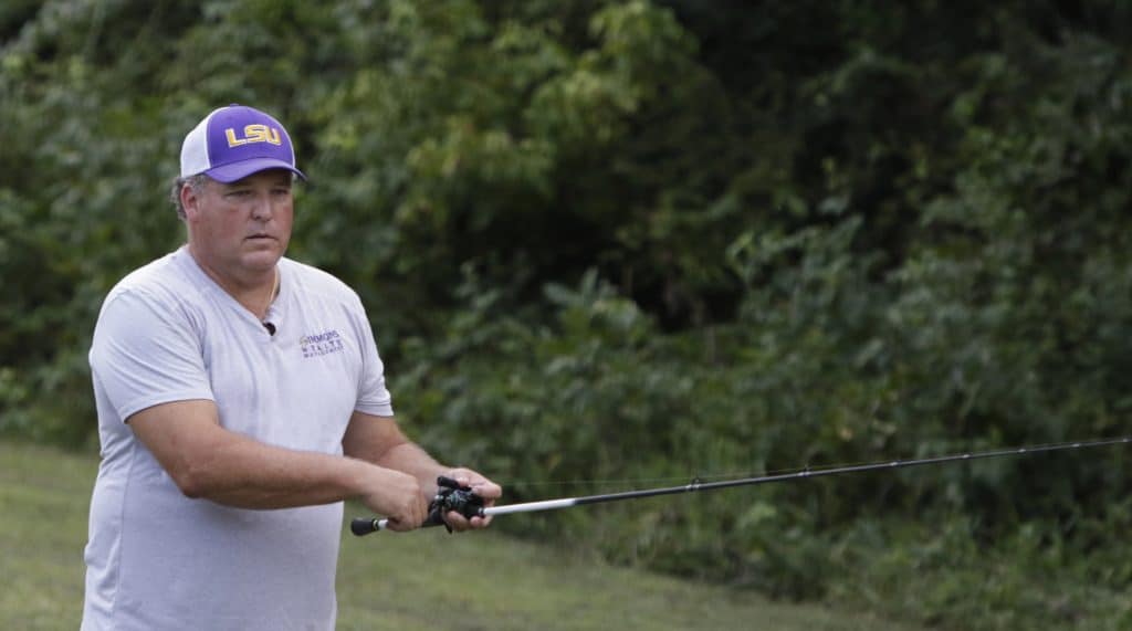 Louisiana native Todd Simmons holding out a fishing line and wearing an LSU hat