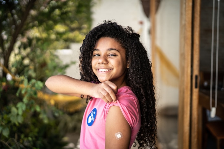 A young girl holds up her shirt to the camera to show a vaccine bandage, used to explain vaccine myths