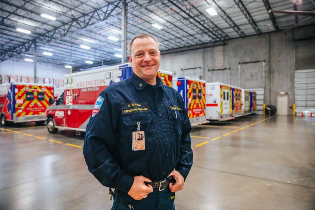 Paramedic and EMS operations manager Michael Marsh smiling at the camera for a photograph with ambulances parked in the background