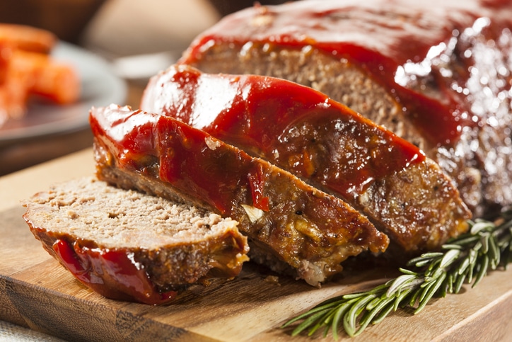 Meatloaf with glaze on a wooden serving board with a sprig of rosemary on the side