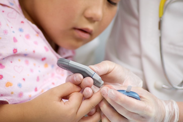 A medical professional in a white coat checks a glucose monitor for a child with diabetes