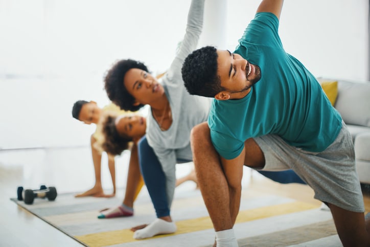 A family of four doing yoga with their left arms stretched in the air 