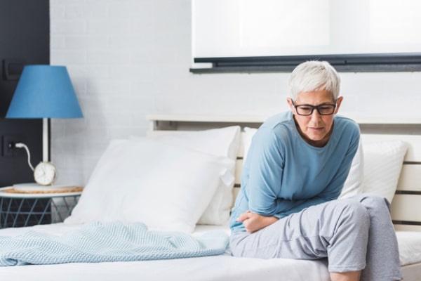 Woman sits on edge of a bed holding her stomach