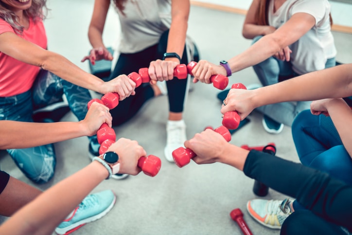 A group of people holding free weights in a circle in the middle of their bodies