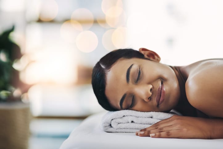 A woman smiling and laying her head on a folded town in a spa-like setting