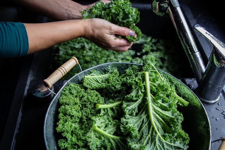 A person washing kale leaves in a sink