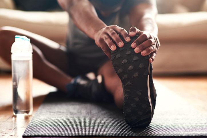 A person grabbing their sneaker and stretching out their leg on a yoga mat