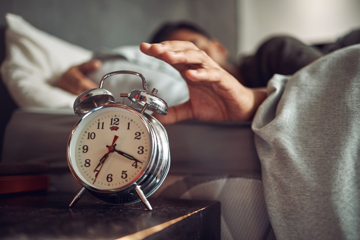 A person reaching for an alarm clock from bed