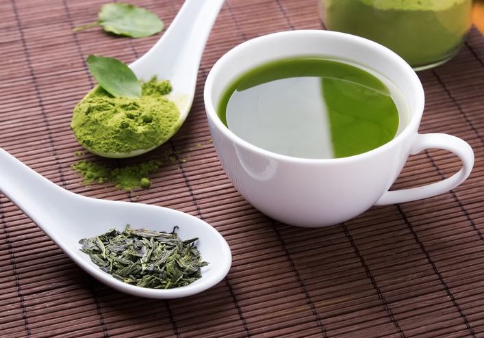 Dried green tea leaves, matcha green tea powder, and a mug of brewed green tea