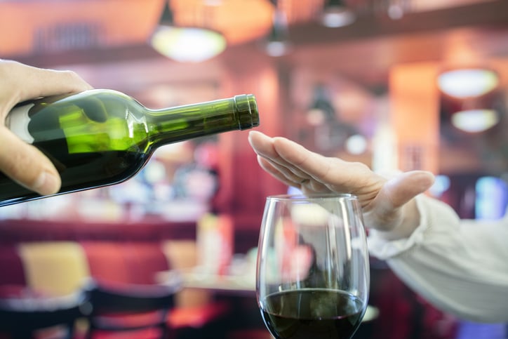 Someone using their hand to block a bottle of wine from pouring into a glass