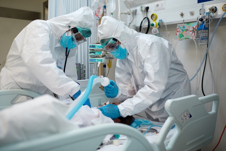 Two fully-dressed medical and surgical professionals caring for a person surrounded by medical equipment 