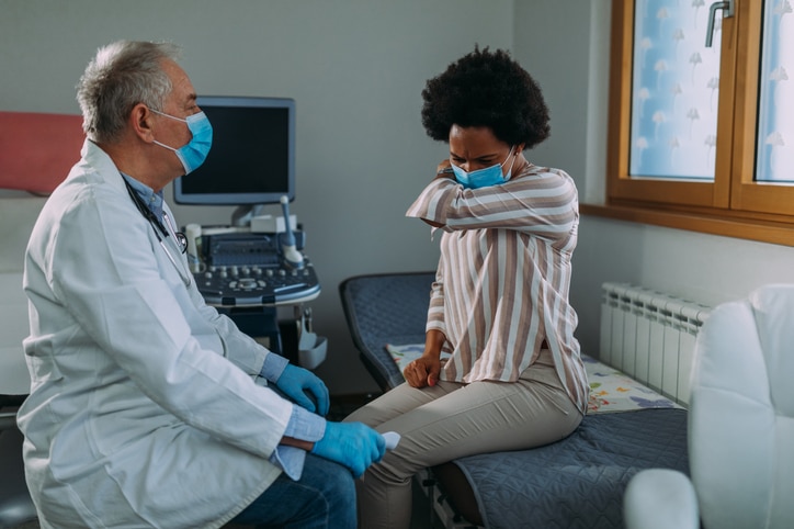 A woman holding her head in her elbow while sitting with a medical professional