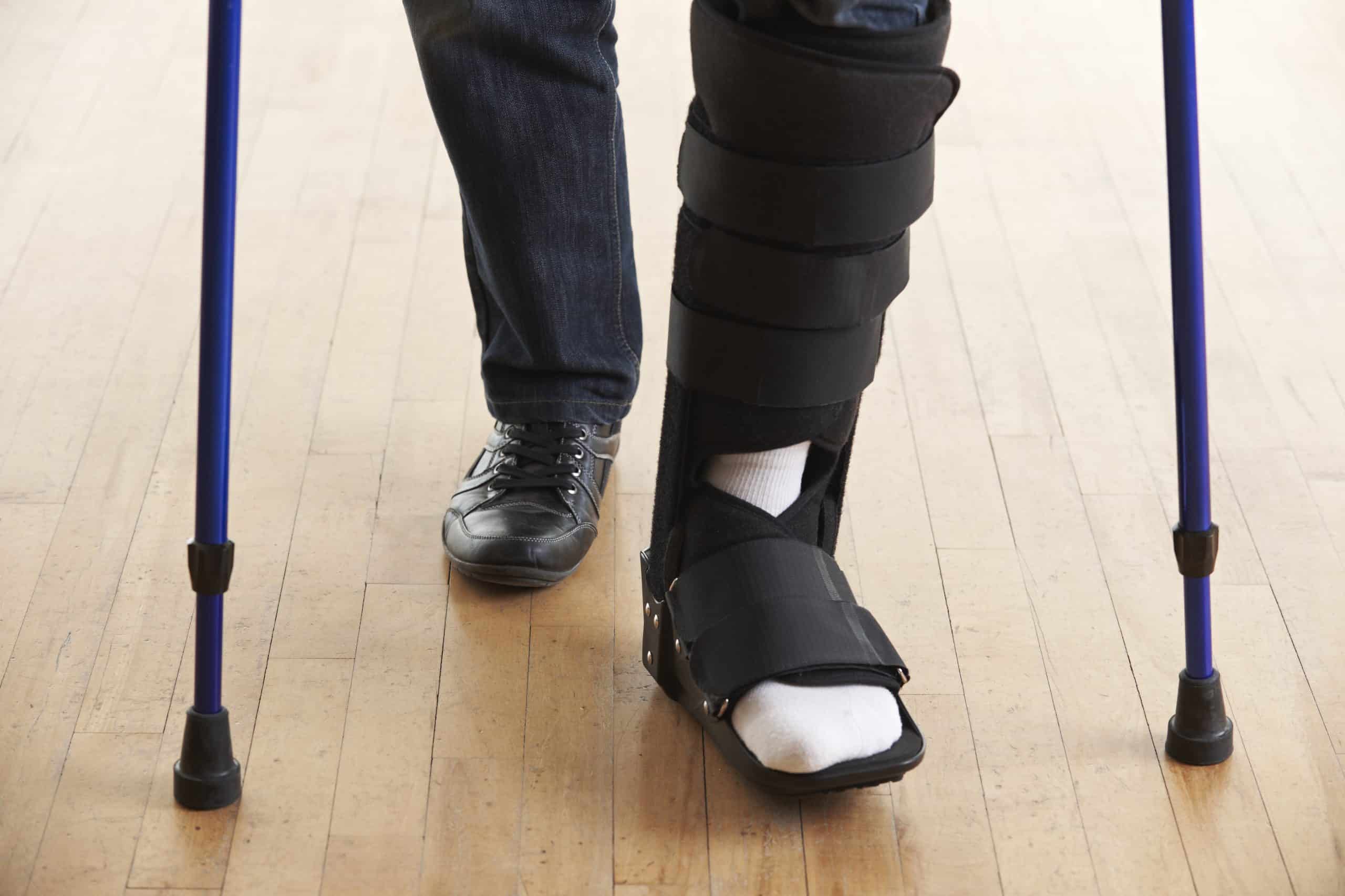 Photo of a foot in a medical boot after an injury with the bottom of a pair of crutches visible