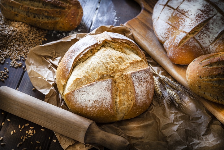 A fresh loaf of a artisan bread with rustic surroundings like wooden rollers and wheat