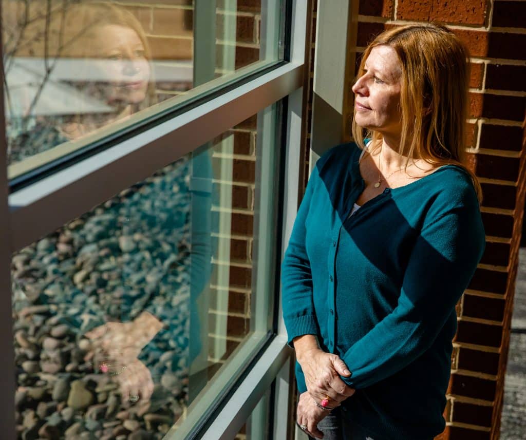 Kim Soesbee looking out a window in front of a brick wall