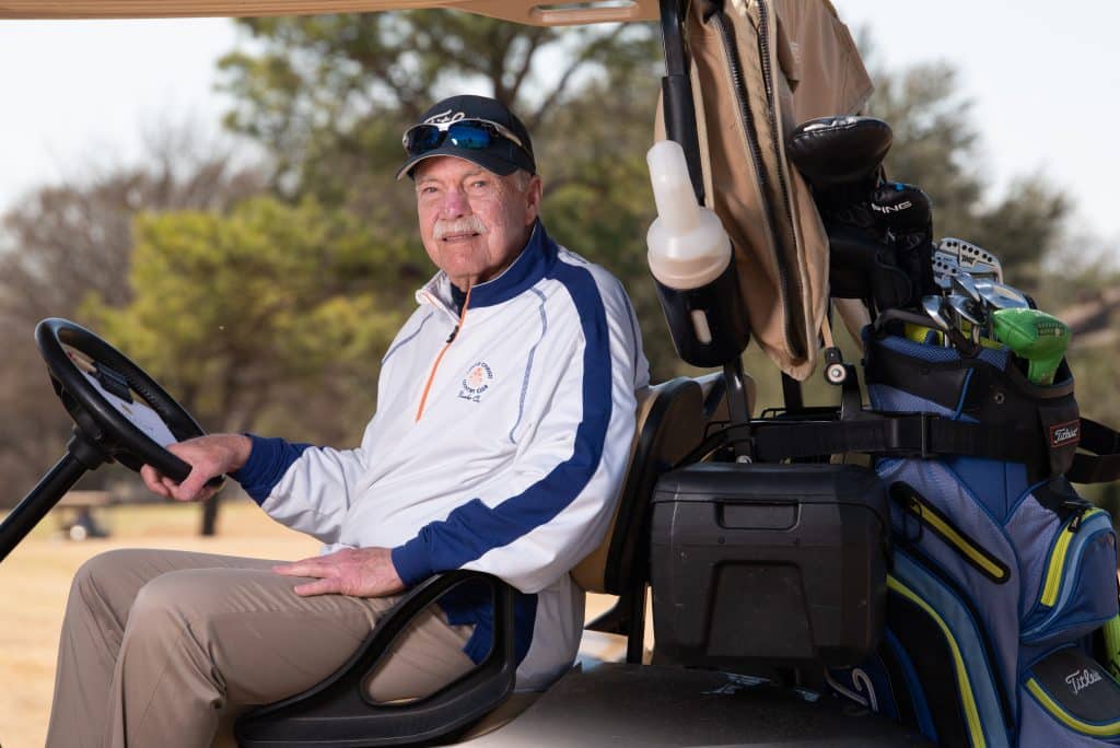 Tom Barrett photographed sitting on a golf cart surrounded by golf equipment 