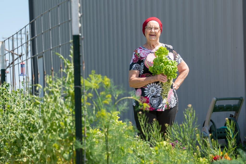 Uterine cancer survivor Mary Nash, wearing a red head wrap and standing in a garden, holds a bundle of greens.