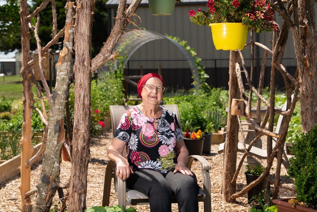 Wearing a red head wrap and a brightly flowered shirt, uterine cancer survivor Mary sits in an arbor on a sunny day.