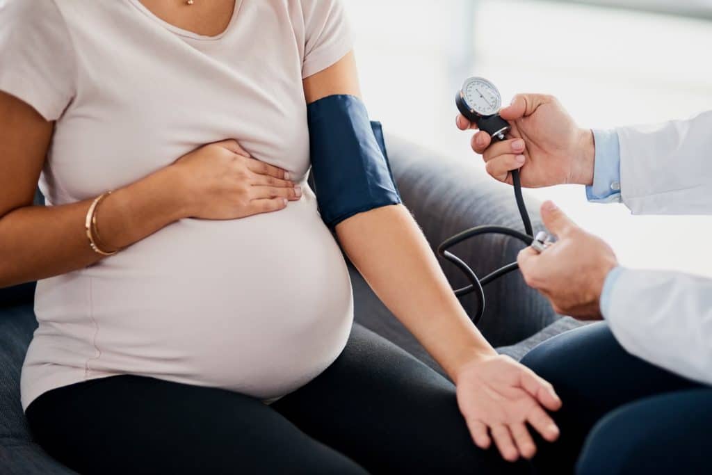 A pregnant woman receiving a blood pressure reading from a medical provider