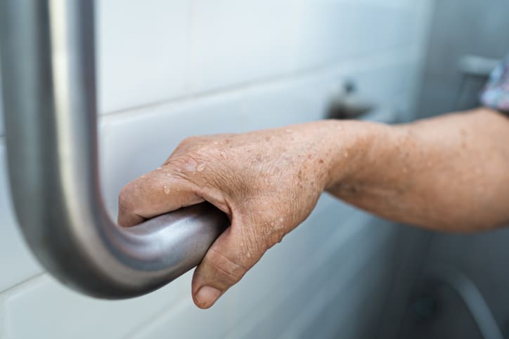 A stock photo of an older person holding onto an assisted bathroom rail