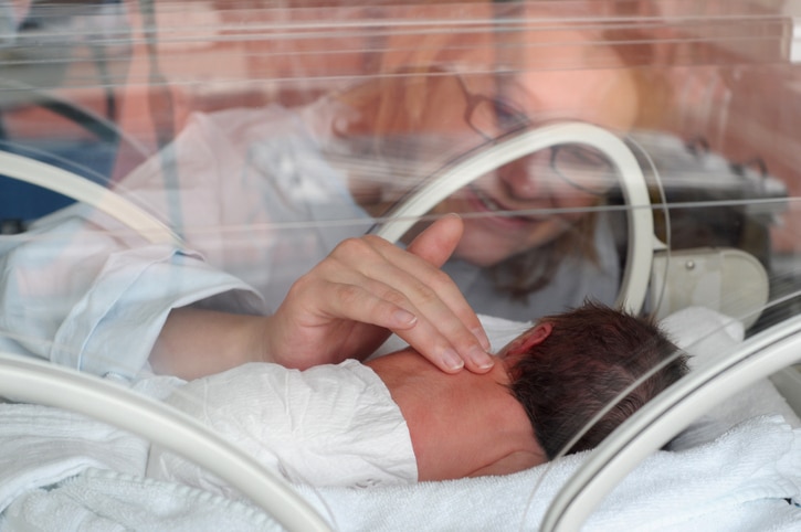 A woman smiling and lightly touching a newborn's back