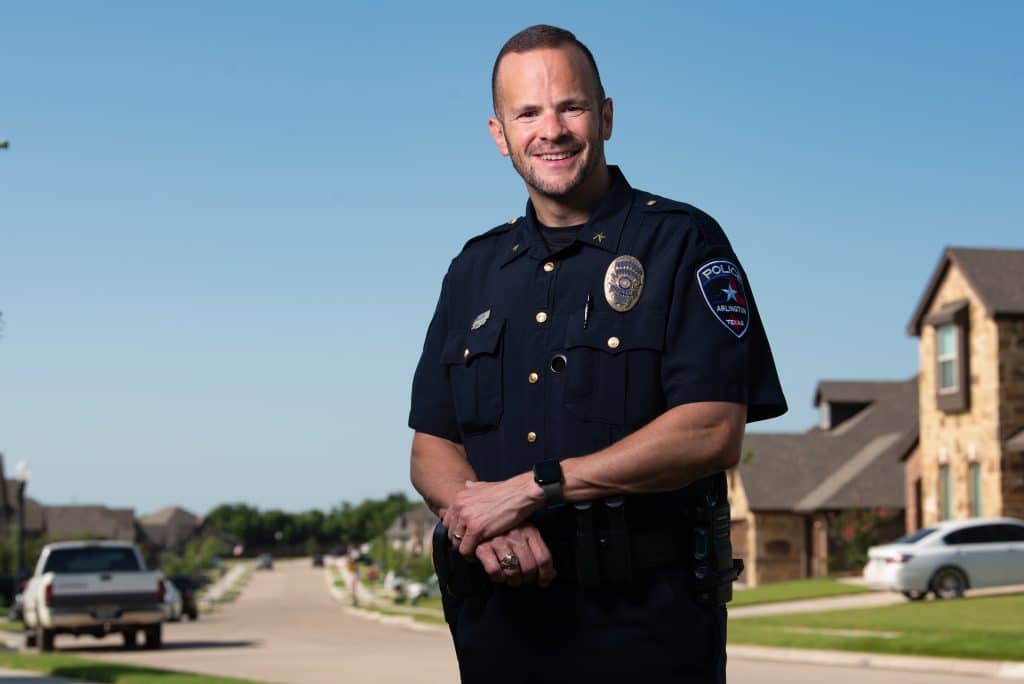 Deputy Chief Brook Rollins standing in his officer uniform, smiling while photographed for a picture, and standing on a suburban neighborhood sheet