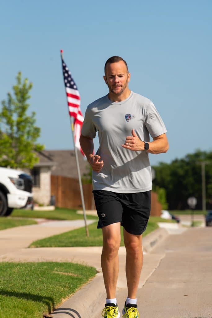 Deputy Chief Brook Rollins running in a gray shirt and black shorts with an American flag in the background
