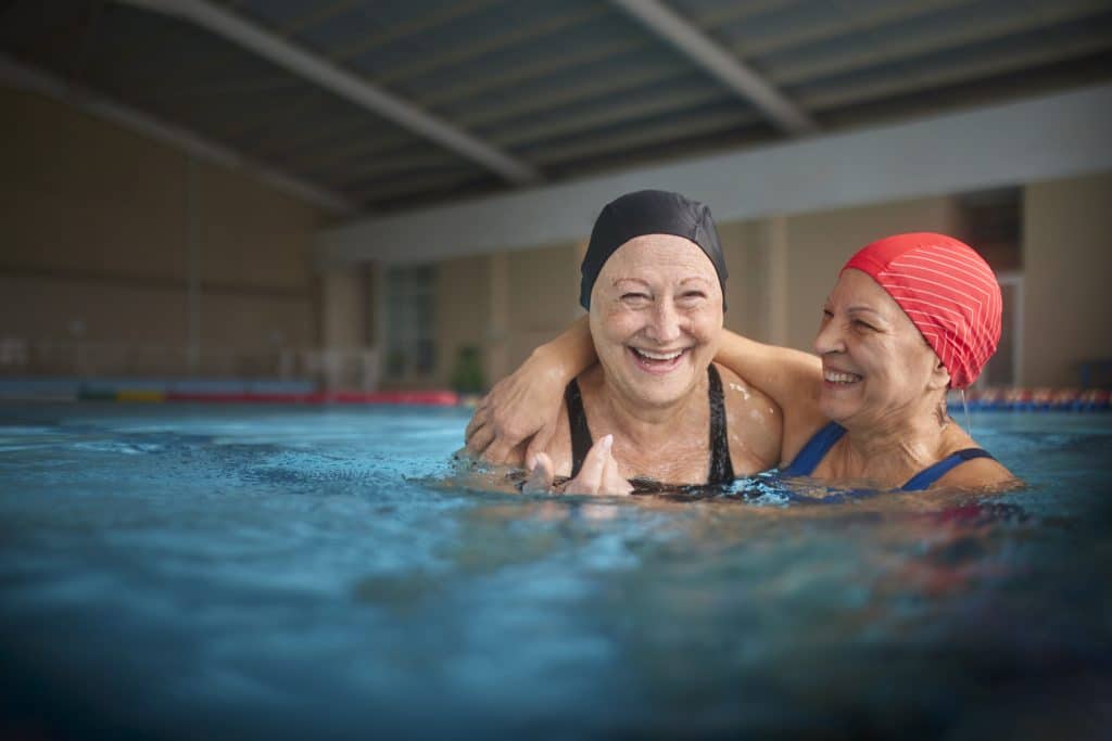 Two people smiling and hugging each other in a pool with swim caps on