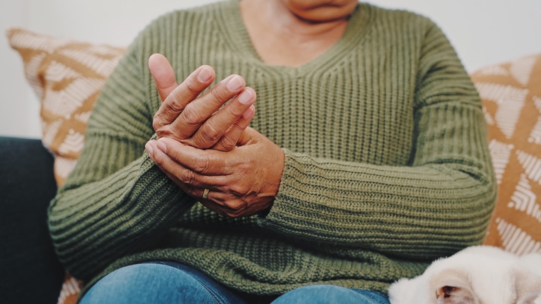 A person wearing a green sweater holding their hands used to explain the link between arthritis and weight gain