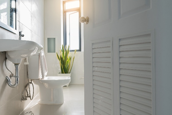 A well-lit bathroom with white walls, finishings, sink, toilet, and floor, shot through a half-closed white door