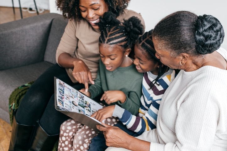 A family, inferred as a mother, grandmother, and two grandchildren, looking through a book of photos