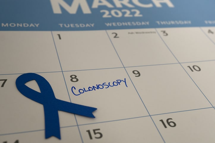 A zoomed in photo of a calendar from March 2022 with a blue ribbon next to the entry for the 8th of the month with the word "Colonoscopy" written in blue ink on that date in all capitals