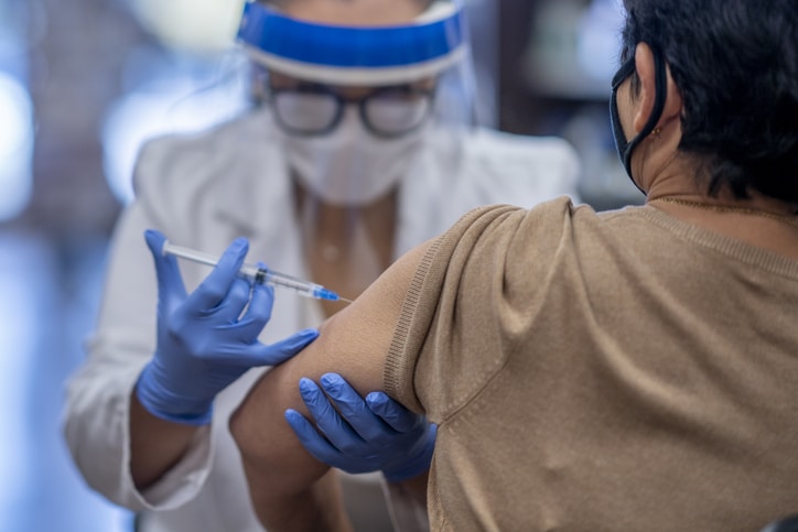 A medical professional wearing PPE administering a vaccine to a patient