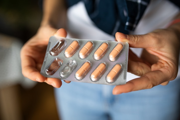 Someone holding a container of beige pills, with three of them taken out