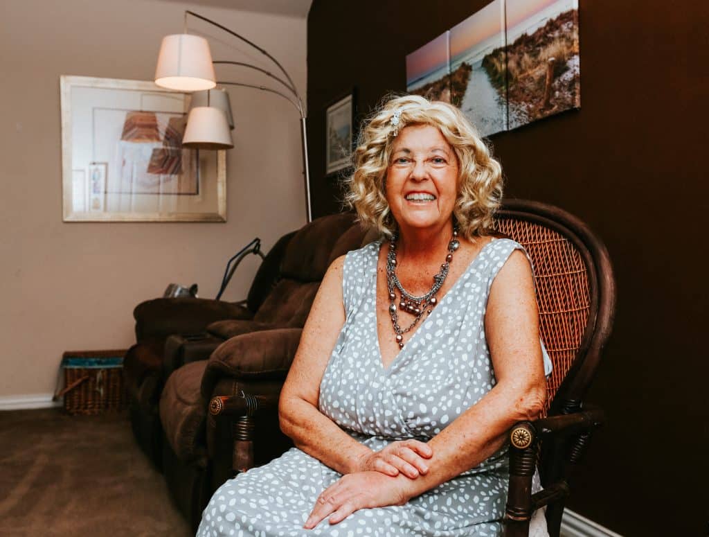 Jeannie Heilman smiling at the camera while sitting in a brown wicker chair