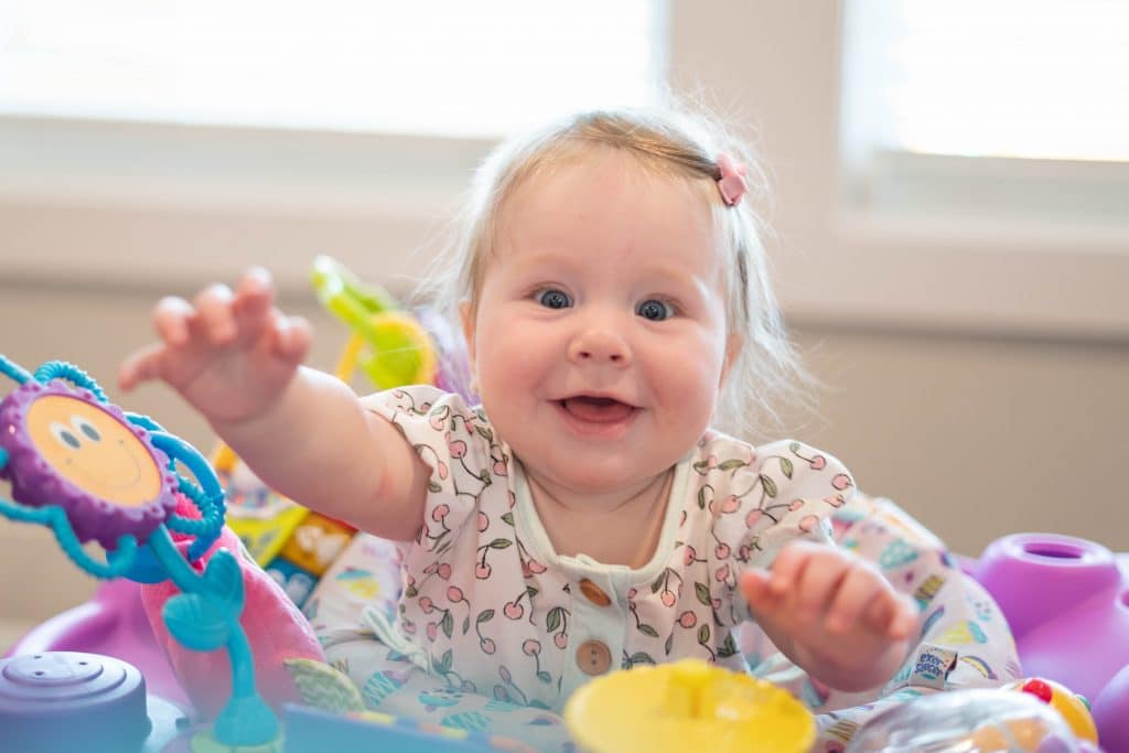 Baby Everleigh playing with toddler toys and reaching toward the camera