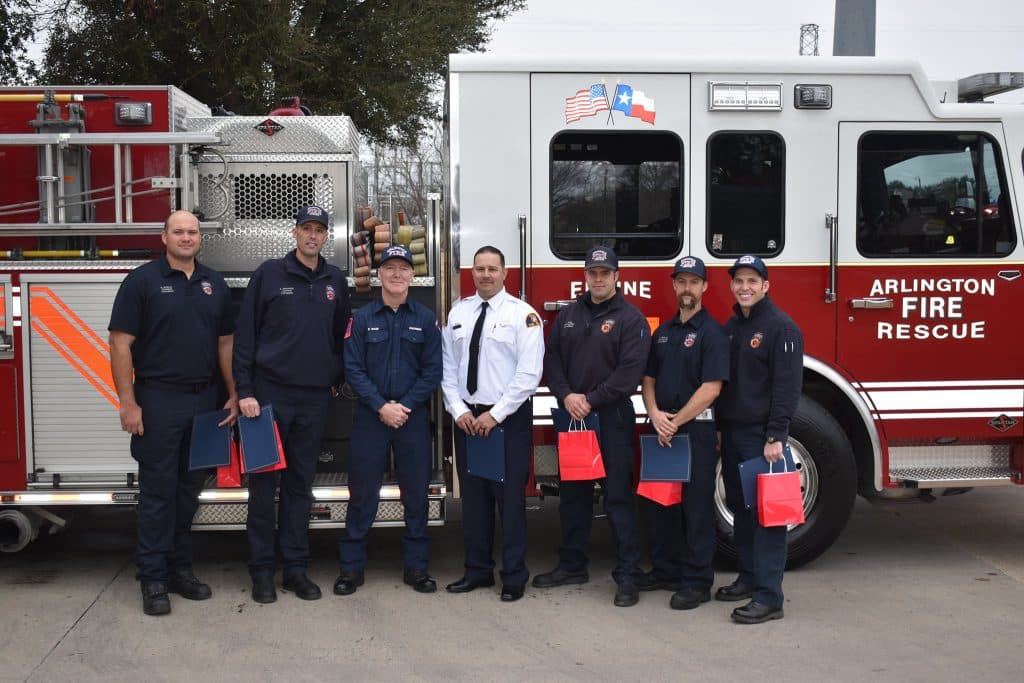 Michael Gonzalez (in white) photographed with Eric Mask (third from left) and other firefighters in front of a fire truck labelled "Arlington Fire Rescue"