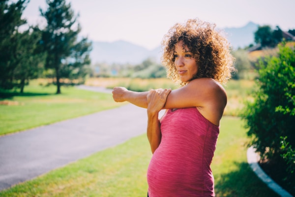 Pregnant woman wearing pink activewear tank top stretching her left arm across her body